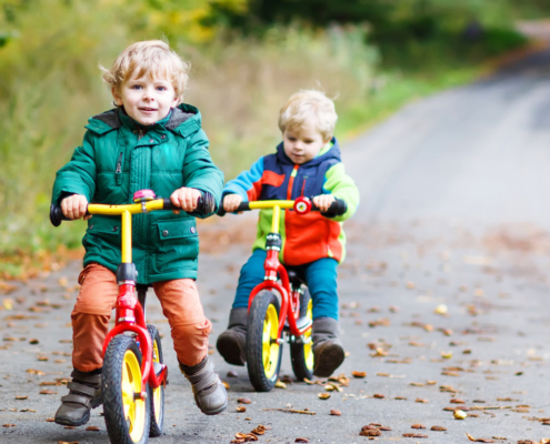 zwei kleine Jungen mit bunten Laufrädern auf einer Straße im Wald