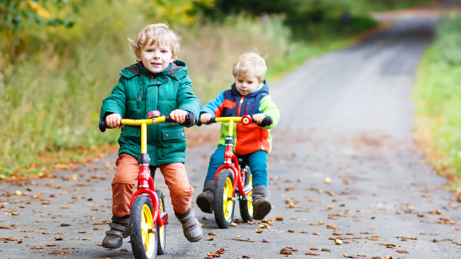 zwei kleine Jungen mit bunten Laufrädern auf einer Straße im Wald