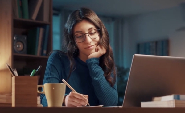 Frau beim Lernen vor einem Monitor, schreibt etwas.